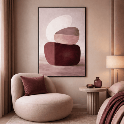 Abstract burgundy and blush Framed Canvas above a cream lounge chair in a softly lit bedroom