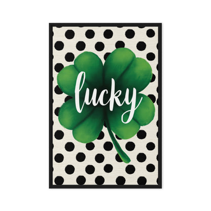 Close view of a green four-leaf clover and white lucky lettering on a black and white polka-dot background